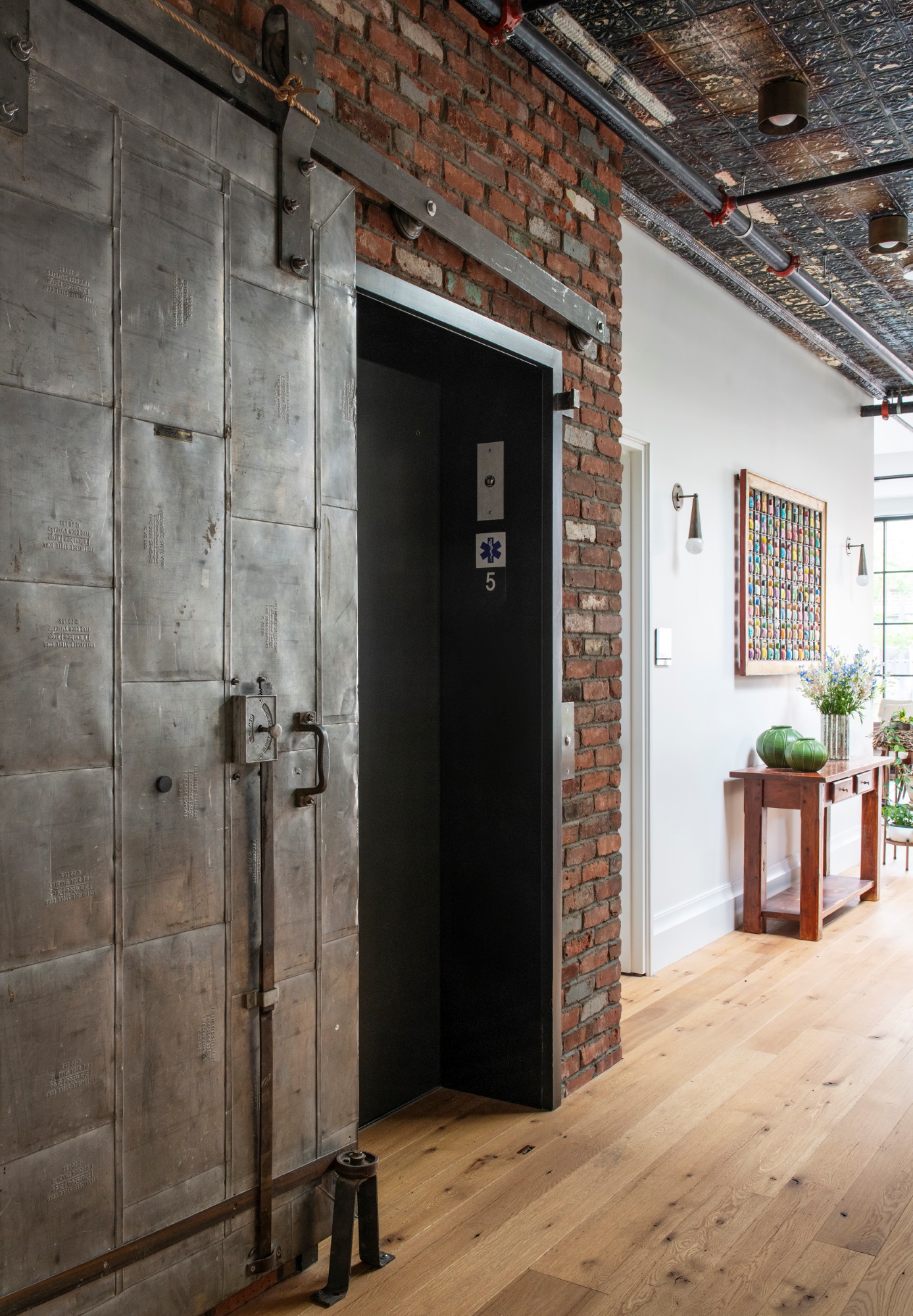 Elevator in a Manhattan apartment with an antique metal barn door and exposed brick wall.